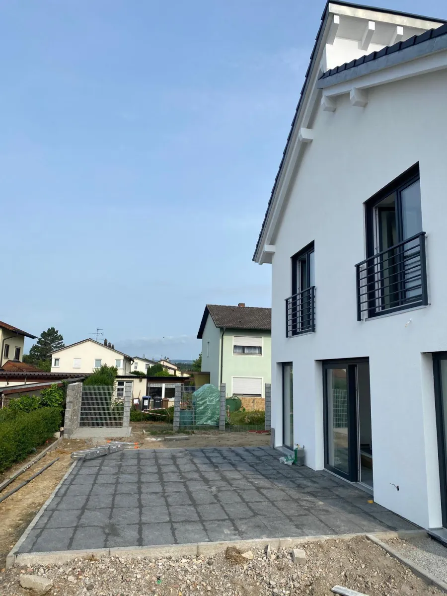 Neubau mit weißer Fassade, Fenstergeländern und neu verlegter Terrassenpflasterung