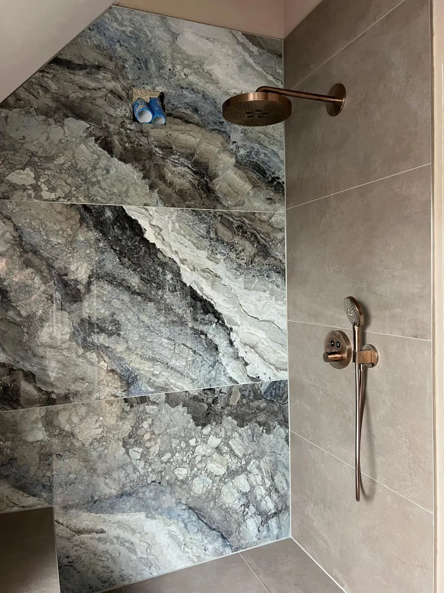 Duschwand mit großformatigen Marmorplatten und Armaturen in Bronze-Optik